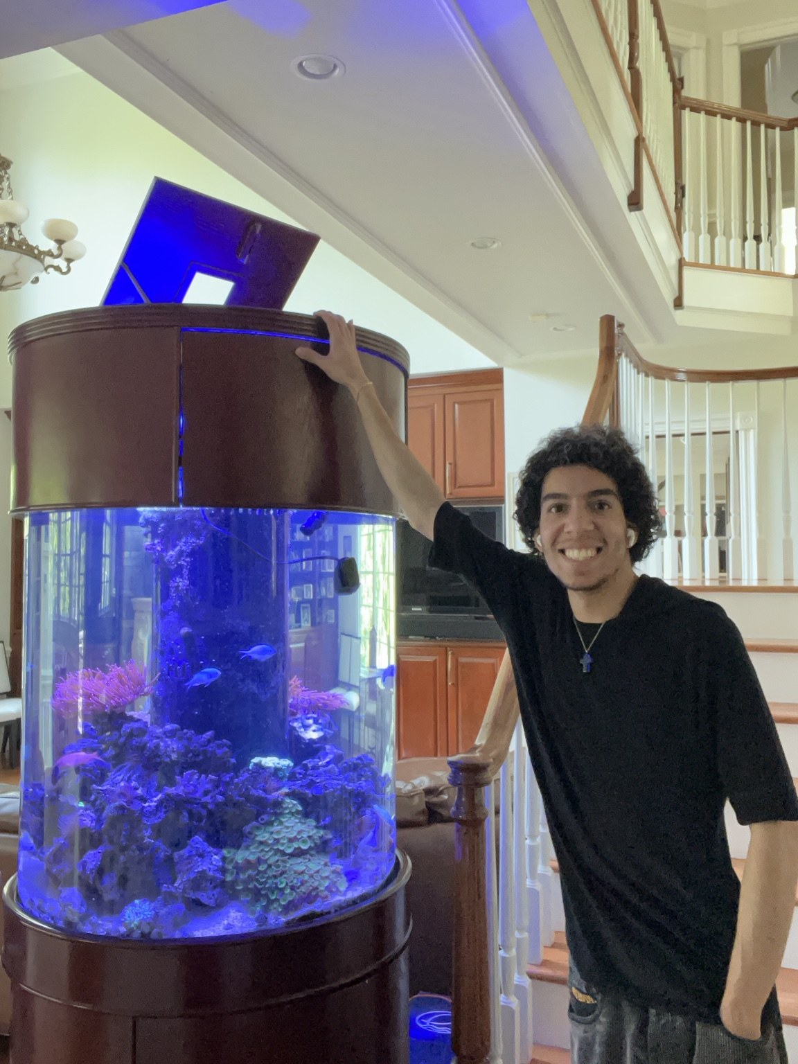 Alkiviades standing beside a private cylindrical reef aquarium